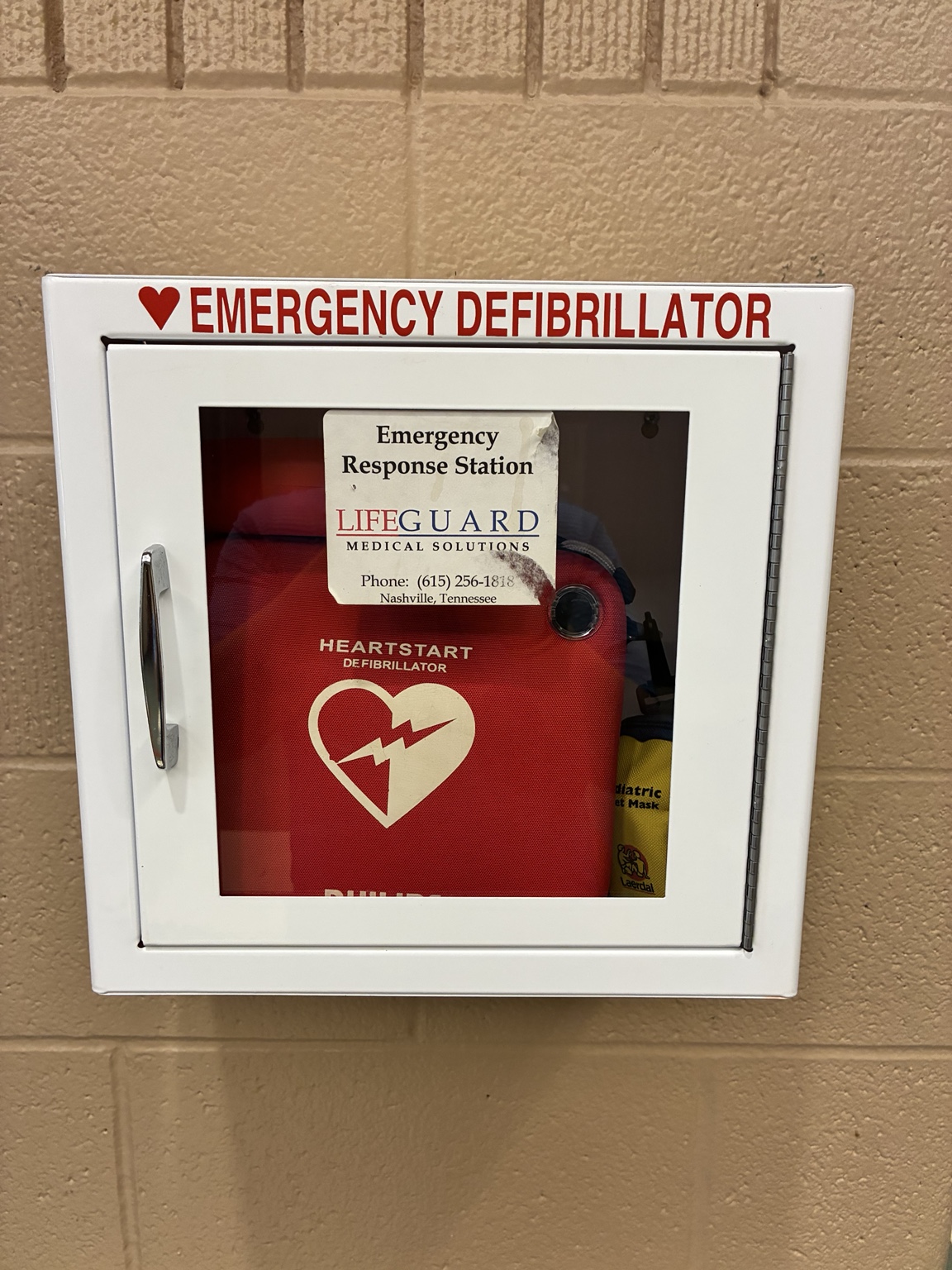 Wall-mounted emergency defibrillator cabinet containing a Philips HeartStart AED