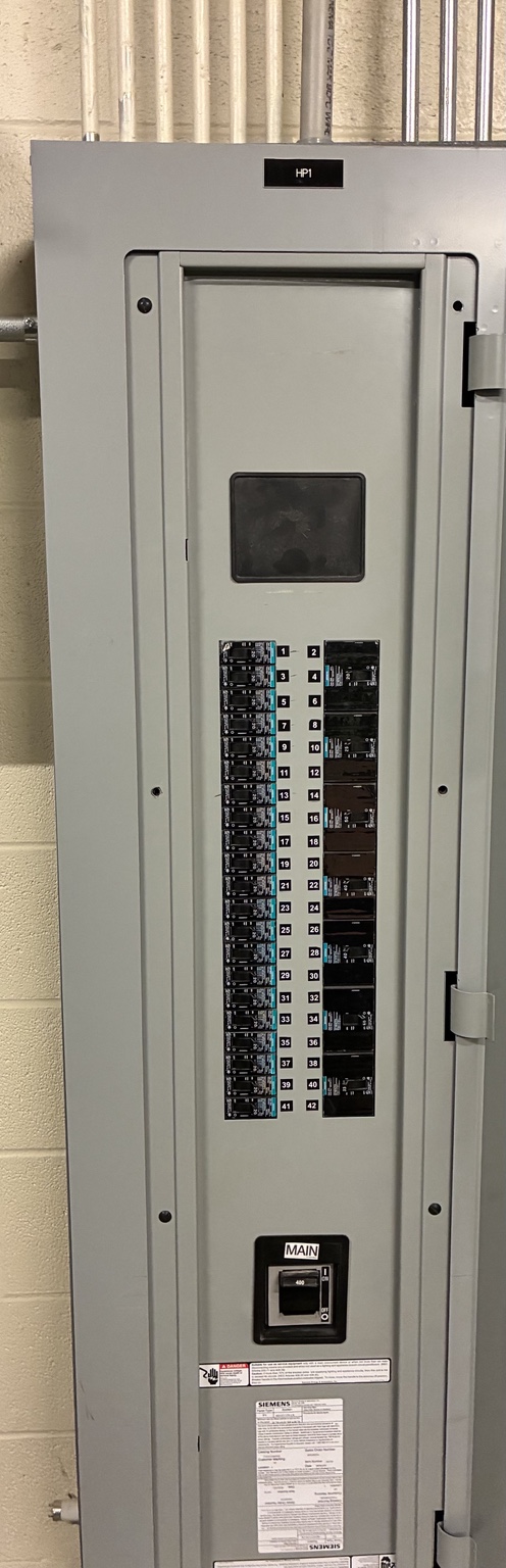 Closed commercial electrical distribution panel with branch circuit breakers and main breaker visible through the dead-front openings