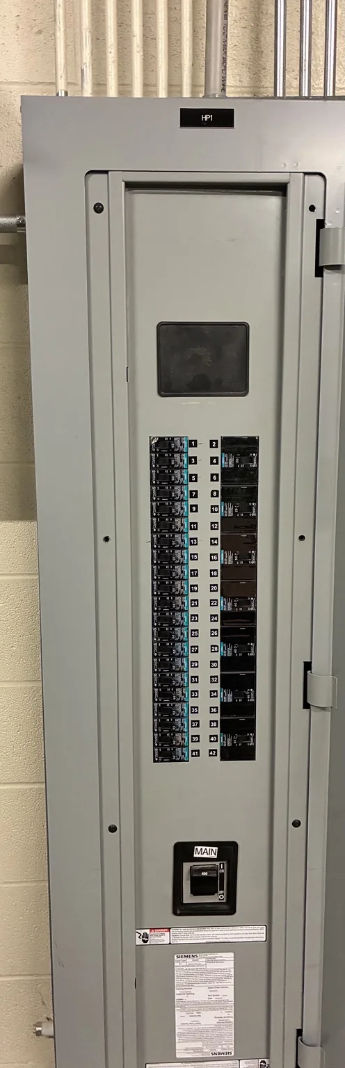 Tablero comercial de distribución eléctrica cerrado, con interruptores de circuitos derivados y el interruptor principal visibles a través de las aberturas de la cubierta interior de protección (dead front)