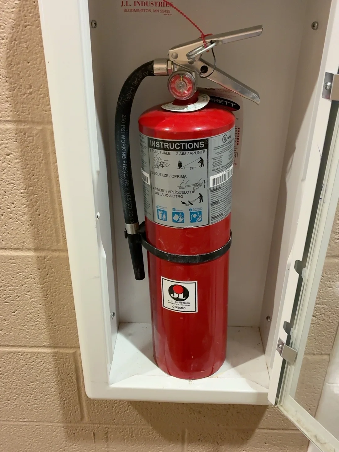 Extintor de incendios portátil montado en un gabinete de pared con manómetro, manguera, etiqueta de funcionamiento, pasador y sello de seguridad visibles